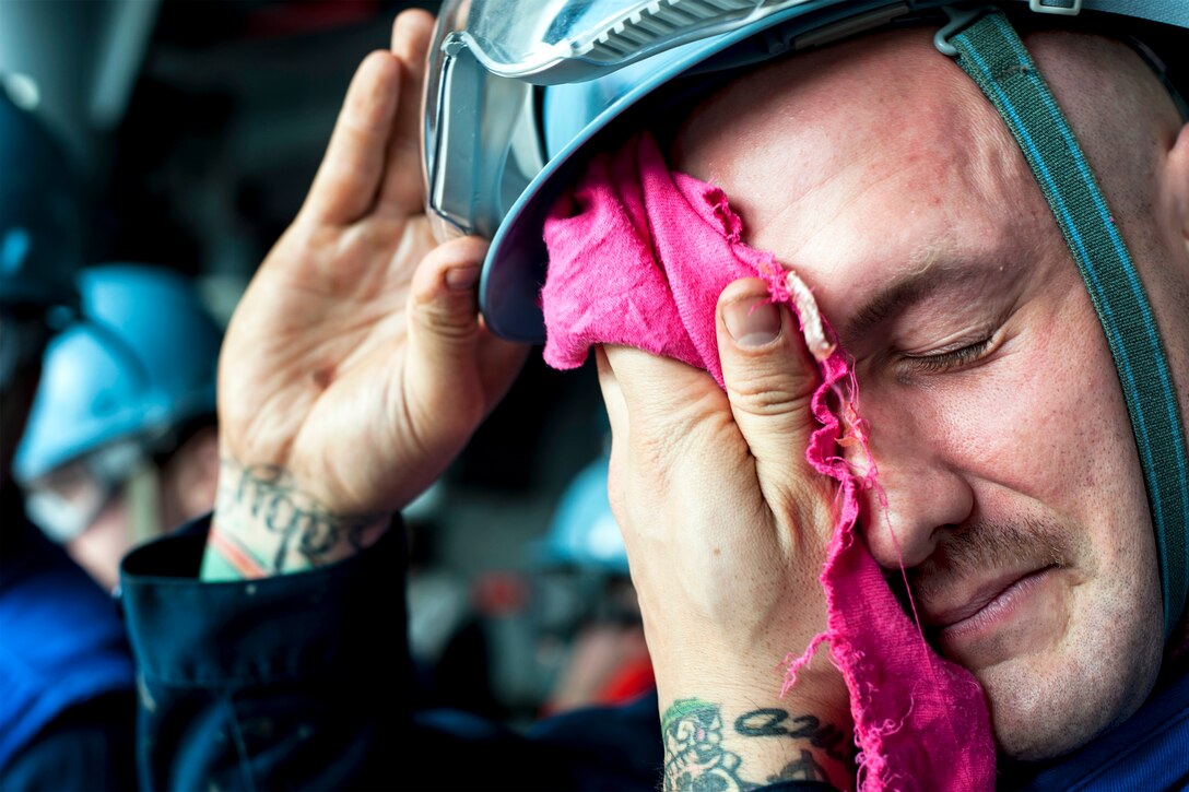 U.S. Navy Petty Officer 2nd Class Joshua Dingman wipes sweat off of his face in a fueling station aboard the aircraft carrier USS George Washington during a replenishment at sea with the USNS Yukon in waters west of the Korean Peninsula, Oct. 14, 2013. Dingman is a boatswain's mate.