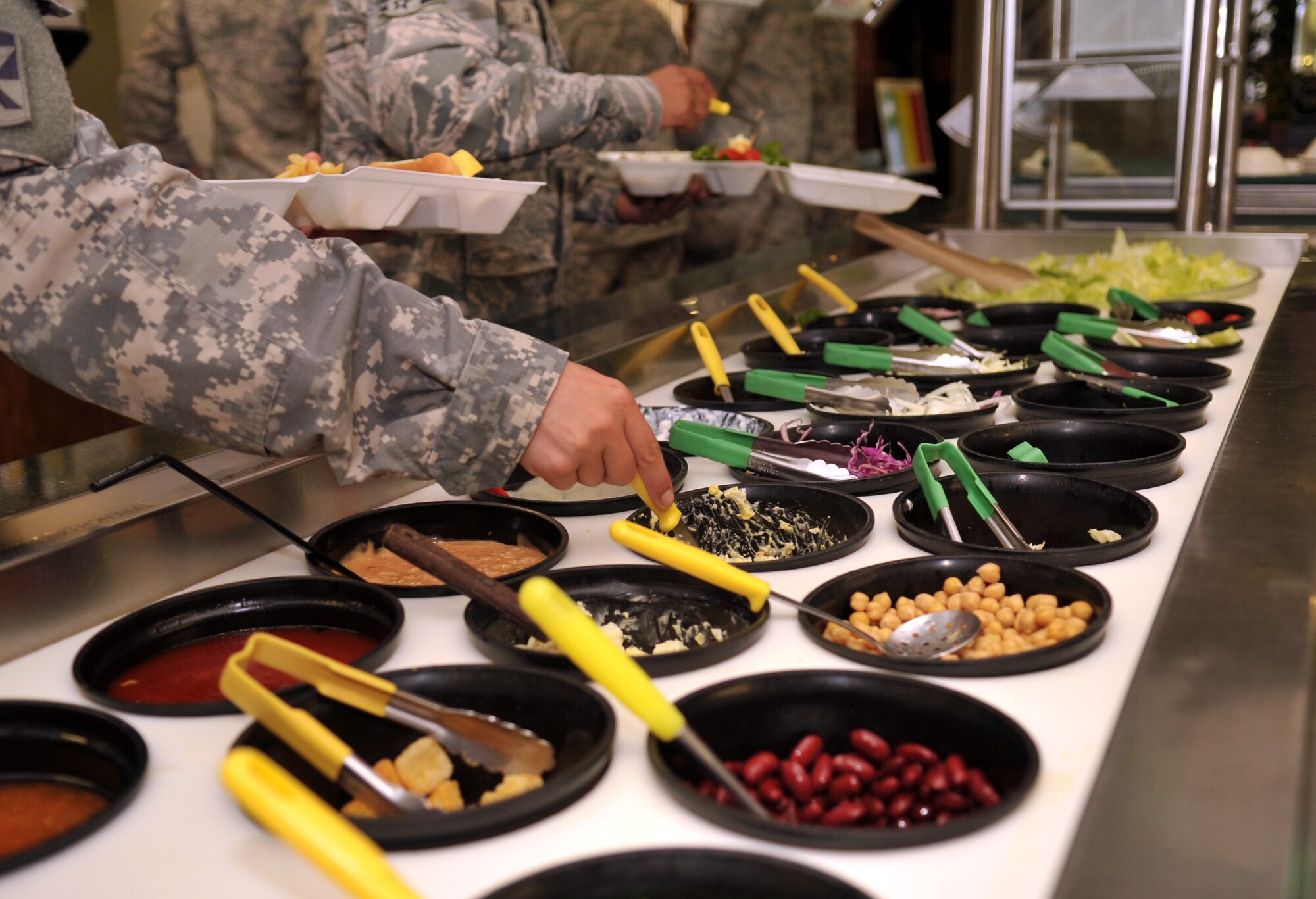 Customers select toppings at the salad bar in the Marshall Dining Facility on Kadena Air Base, Japan, Oct. 17, 2013. The DFAC has a variety of meal choices that include fresh fruits and vegetables and an open salad bar. (U.S. Air Force photo by Naoto Anazawa)