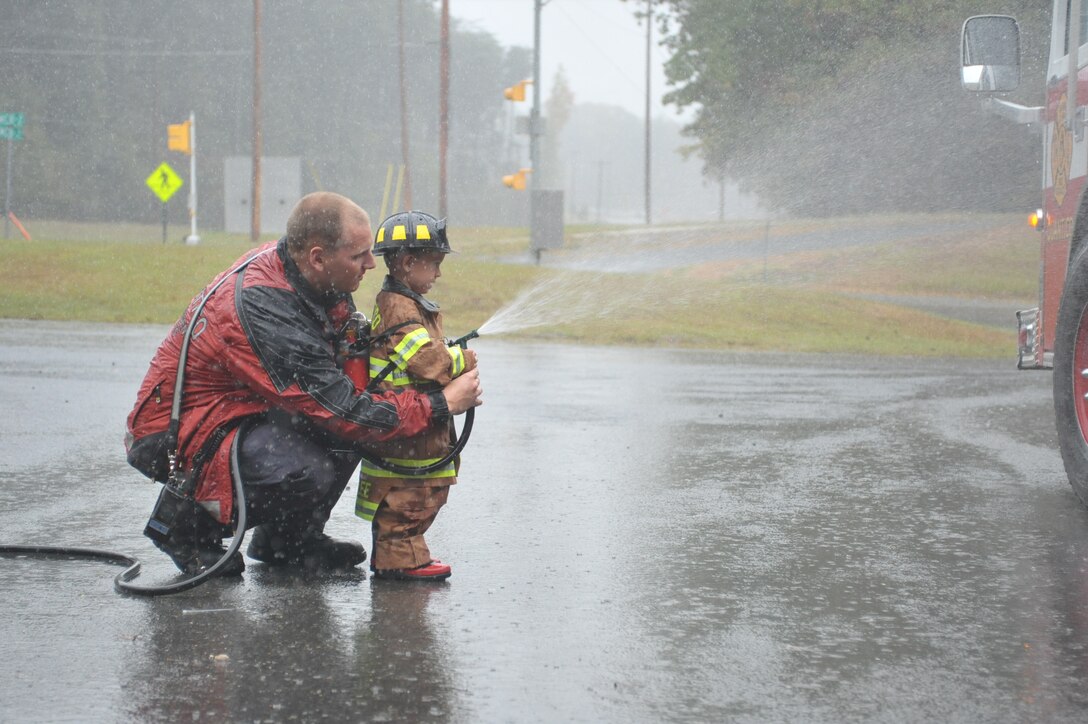 Tommy, 3 hoses down a fire truck with the help of Austin Oakley, firefighter, Quantico Fire and Emergency Services, while at Fire Station 533 on Oct. 10, 2013. TJ is a 3-year-old who has Langerhan cell histiocytosis. 