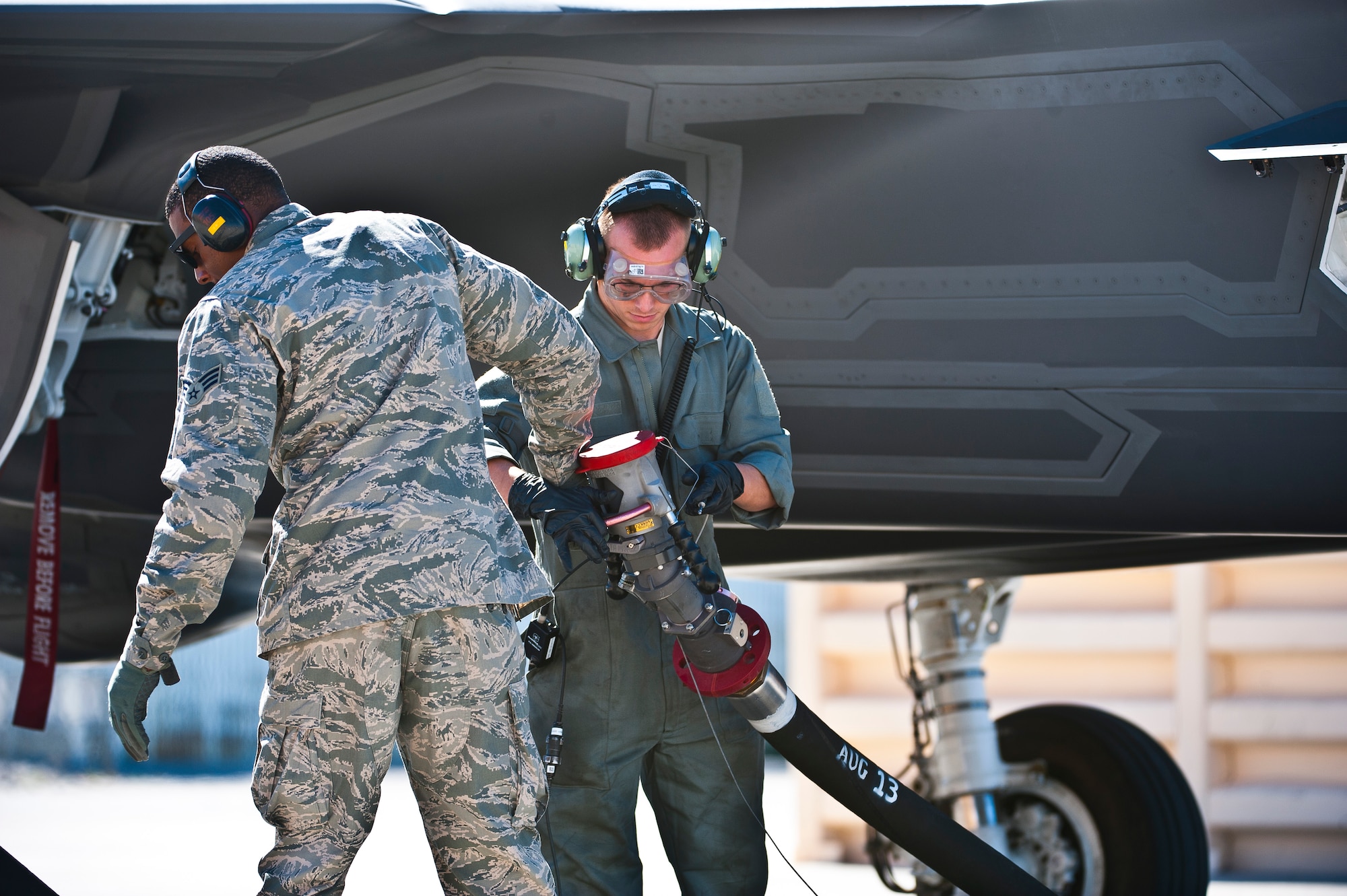 Senior Airman Kyle Hood II (left), 99th Logistics Readiness Squadron fuels management specialist, retrieves a fuel hose from Staff Sgt. Nicholas Fagerstrom, 57th Aircraft Maintenance Squadron crew chief, after refueling an F-35 Lightning II at the revetments Oct. 16, 2013, at Nellis Air Force Base, Nev. Refueling specialists and crew chiefs assigned to the 57th AMXS and 99th Logistics Readiness Squadron practice this procedure to keep their skills sharp and aid in the effort to provide combat-ready air power at a moment’s notice. (U.S. Air Force photo by Senior Airman Brett Clashman)
