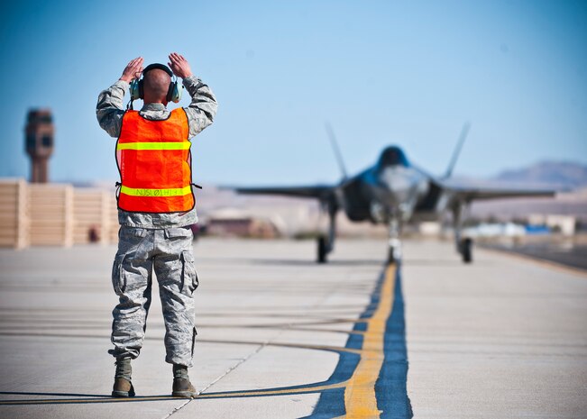 Staff Sgt. William Rispoli, 57th Aircraft Maintenance Squadron aerospace propulsion specialist, marshals an F-35 Lightning II at the revetments Oct. 16, 2013, at Nellis Air Force Base, Nev. The F-35 is a single-seat, single-engine, fifth-generation multirole fighter that performs ground attack, reconnaissance, and air defense missions with stealth capability. (U.S. Air Force photo by Senior Airman Brett Clashman)