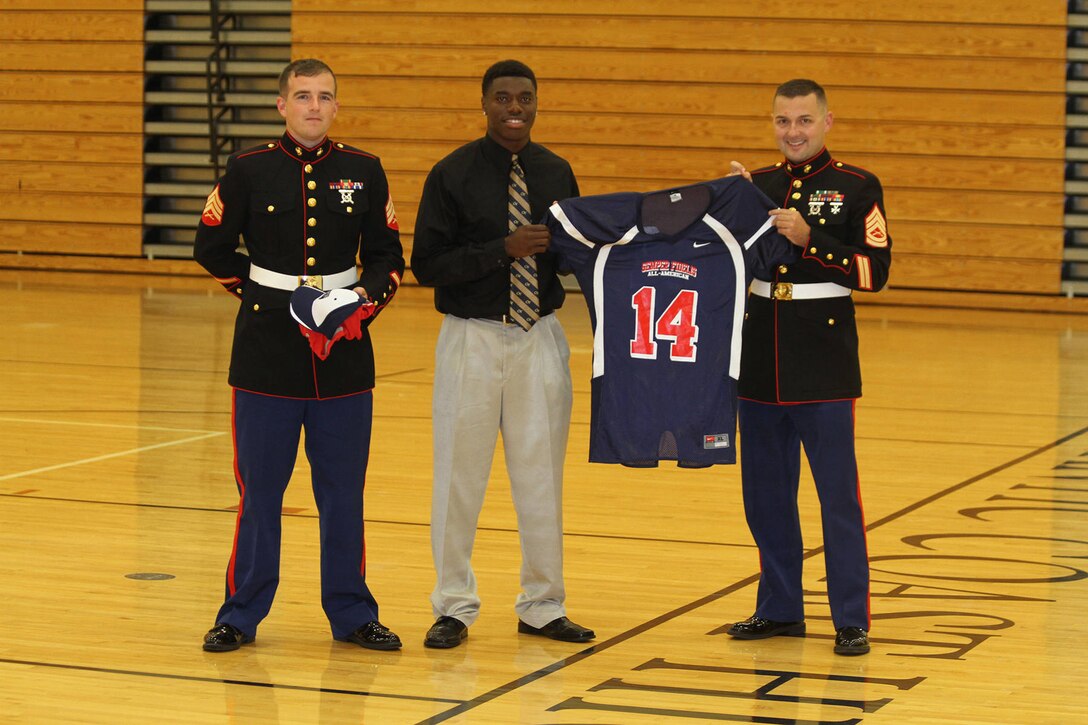 Sgt. Colin C. Seeley (Left) and Gunnery Sgt. Tyler D. Mitchell, two recruiters with Recruiting Station Jacksonville, present a Semper Fidelis All-American Bowl Jersey to Stepheny Durham at Atlantic Coast High School, Fla., Oct. 15, 2013.  The Semer Fi Bowl will take place in Carson, Calif., Jan. 5, 2014.