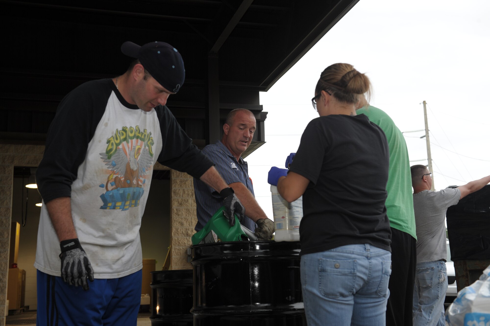 Hurlburt volunteers and Bart Shumaker, center, Shoreline Environmental president, dump liquids such as used oil and contaminated gasoline into a drum for processing during a Household Hazardous Waste Collection Day on Hurlburt Field, Fla., Oct. 18, 2013. More than 300 gallons of oil and fluids were collected during the event. (U.S. Air Force photo/Senior Airman Kentavist P. Brackin)
