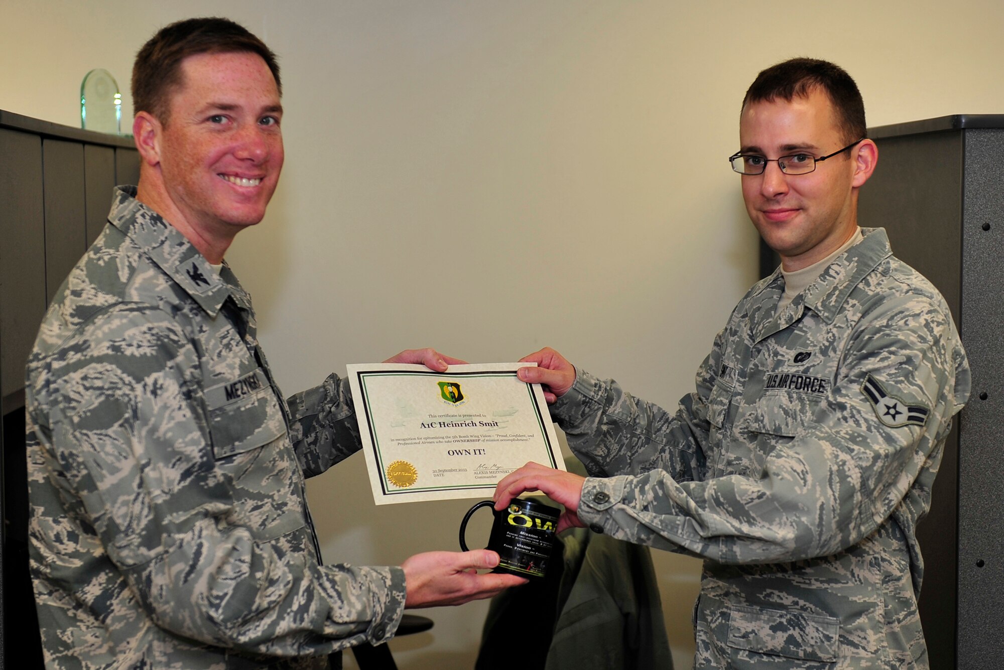 Airman 1st Class Heinrich Smit, 5th Contracting Squadron is presented the Own It Award by Col. Alex Mezynski, 5th Bomb Wing commander, at Minot Air Force Base, N.D., Oct. 22. Smit was recognized for exemplifying the 5th BW vision of “Proud, Confident, and Professional” Airmen who take ownership of mission accomplishment. (U.S. Air Force photo/Senior Airman Kristoffer Kaubisch)