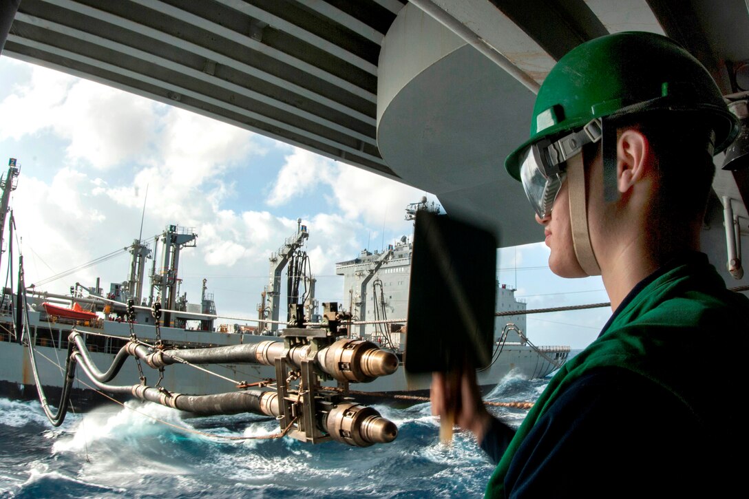 U.S. Navy Seaman Austin Klug signals to the Military Sealift Command fleet replenishment oiler USNS Yukon aboard the aircraft carrier USS George Washington during a replenishment in the South China Sea, Oct. 20. 2013.