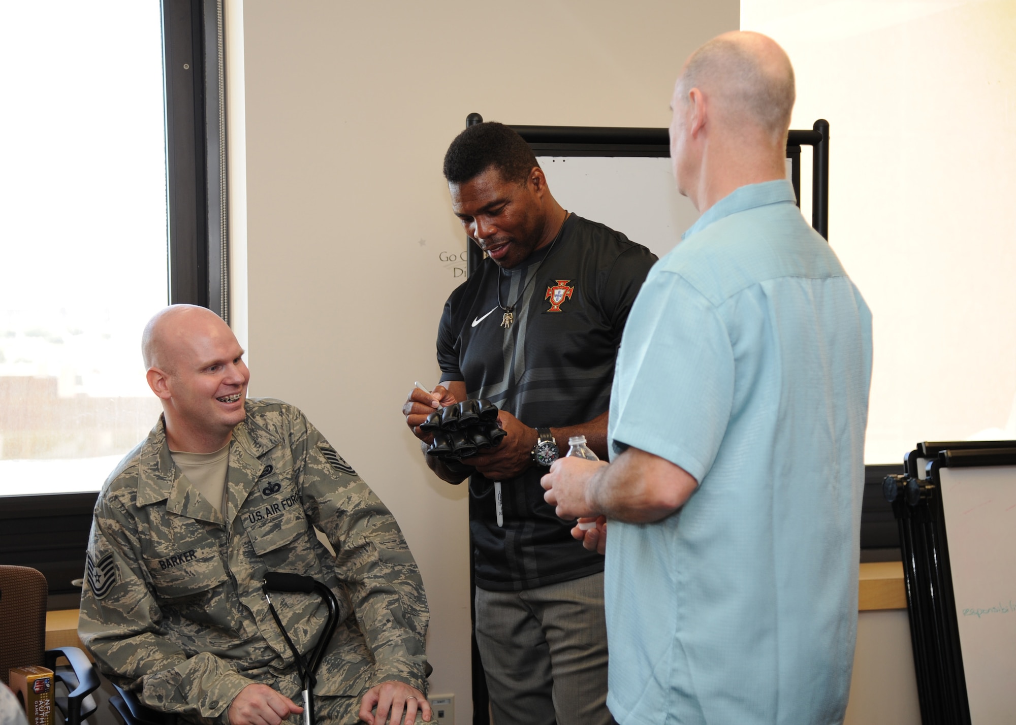 Herschel Walker, center, signs an autograph for Tech. Sgt. Christopher Barker, 59th Medical Wing Patient Squadron, and his father Daniel Barker during a recent visit to the Wilford Hall Ambulatory Surgical Center Oct. 23, 2013, at Joint Base San Antonio-Lackland, Texas. Earlier in the day, Barker was presented with the distinguished Purple Heart for wounds sustained in action. (U.S. Air Force photo/Staff Sgt. Jerilyn Quintanilla)
