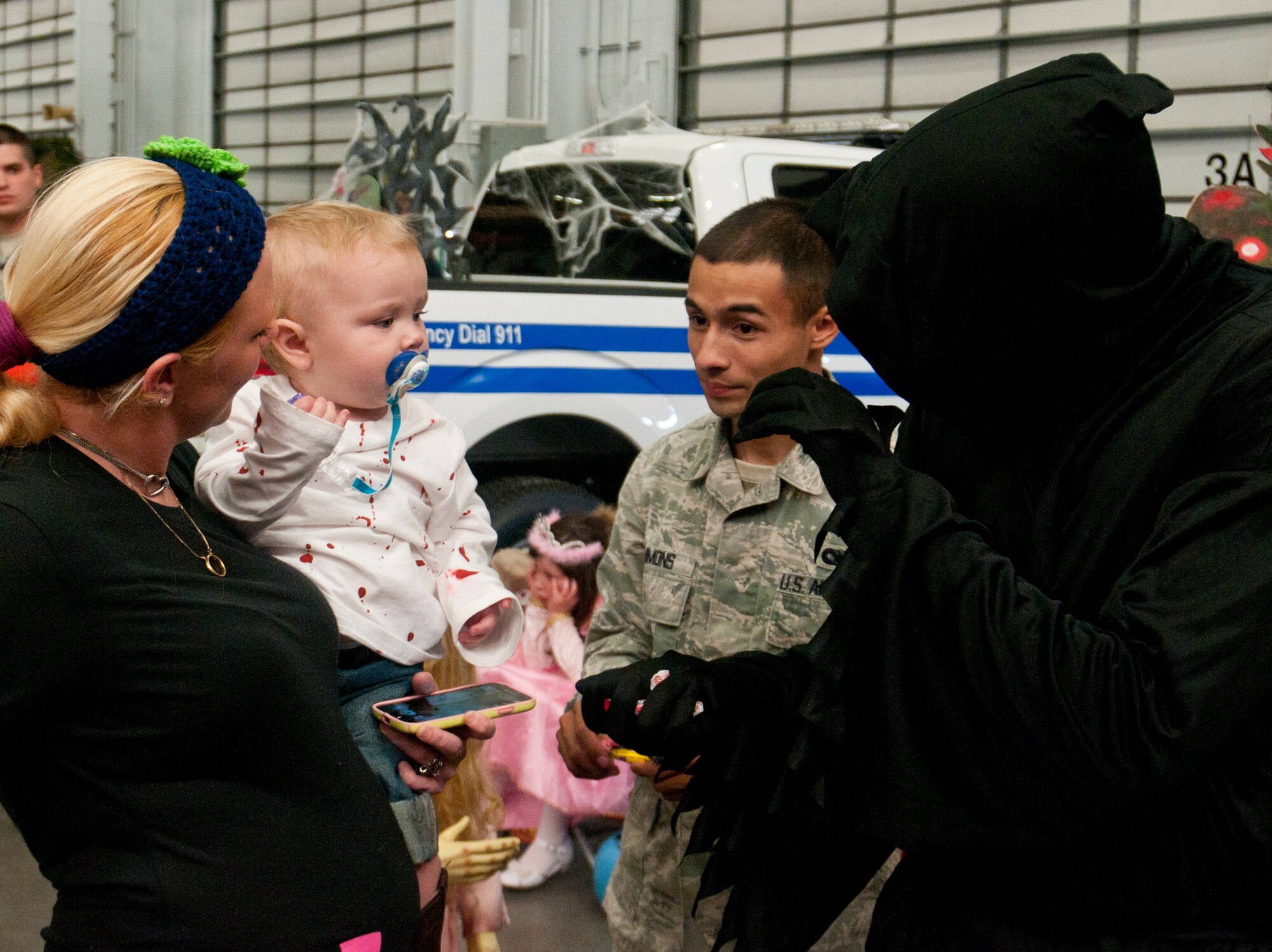 Senior Airman Dean Kaelin, 90th Security Forces Squadron, dressed as a ghoul, hands candy to Tyger Dalton, son of Tech Sgt. Casey Dalton, 90th Security Forces Group Standards and Evaluations, while Tyger’s mother, Tiffany Holihan, holds him at the 90th SFG Trunk-or-treat in Bldg. 1501, Oct. 19, 2013. (U.S. Air Force photo by Airman 1st Class Jason Wiese)