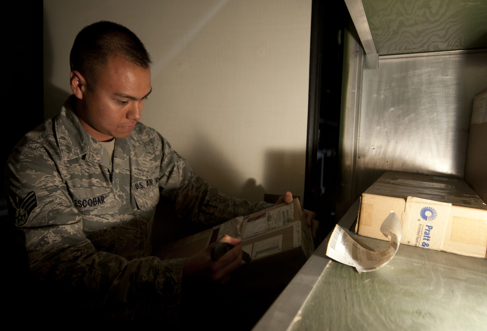 U.S. Air Force Senior Airman Tracy Escobar, 380th Expeditionary Logistics Readiness Squadron flightline supply journeyman, removes old tracking information from a package at an undisclosed location in Southwest Asia Oct. 8, 2013. He removed the old information to avoid confusion when shipped back. Escobar calls Huntington Beach, Calif., home and is deployed from Minot Air Force Base, N.D. (U.S. Air Force photo by Staff Sgt. Jacob Morgan)