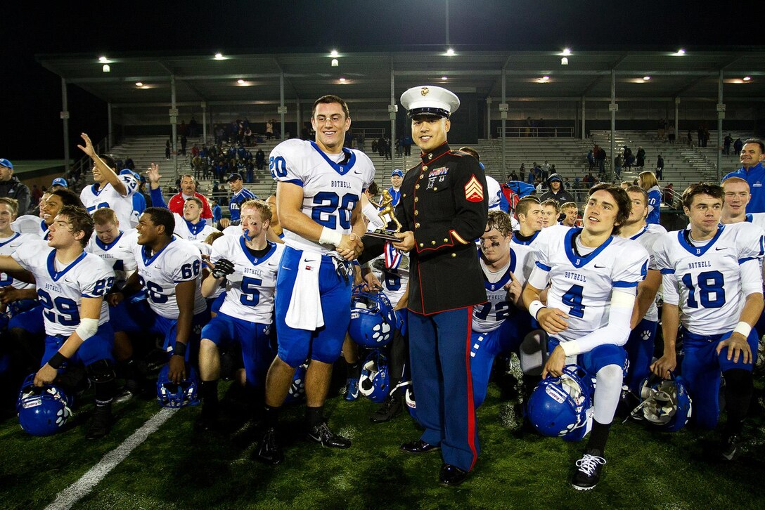Sgt. Erick Fandialan, a recruiter with Marine Corps Recruiting Substation Bellevue, presents the most valuable player trophy to 16-year-old Sam McPherson from Bothell High School following a Great American Rivalry Series football game against Inglemoor High School at Pop Keeney Stadium in Bothell, Wash., Oct. 18, 2013. Bothell HS victored in this year's contest. Fandialan, 27, is from Silverdale, Washington. 