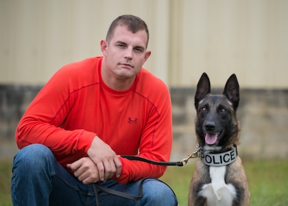Staff Sgt. Timothy Garrett, 628th Security Force K’9 handler, and his dog, Tze, pose for a photo outside a warehouse October 22, 2013 during Explosives detection training in Summerville, S.C. During this training, the dogs undergo obstacles where they searched through blocks or warehouse equipment for substances that are and may be used by terrorists or criminals. (U.S. Air Force/Senior Airman Ashlee Galloway)