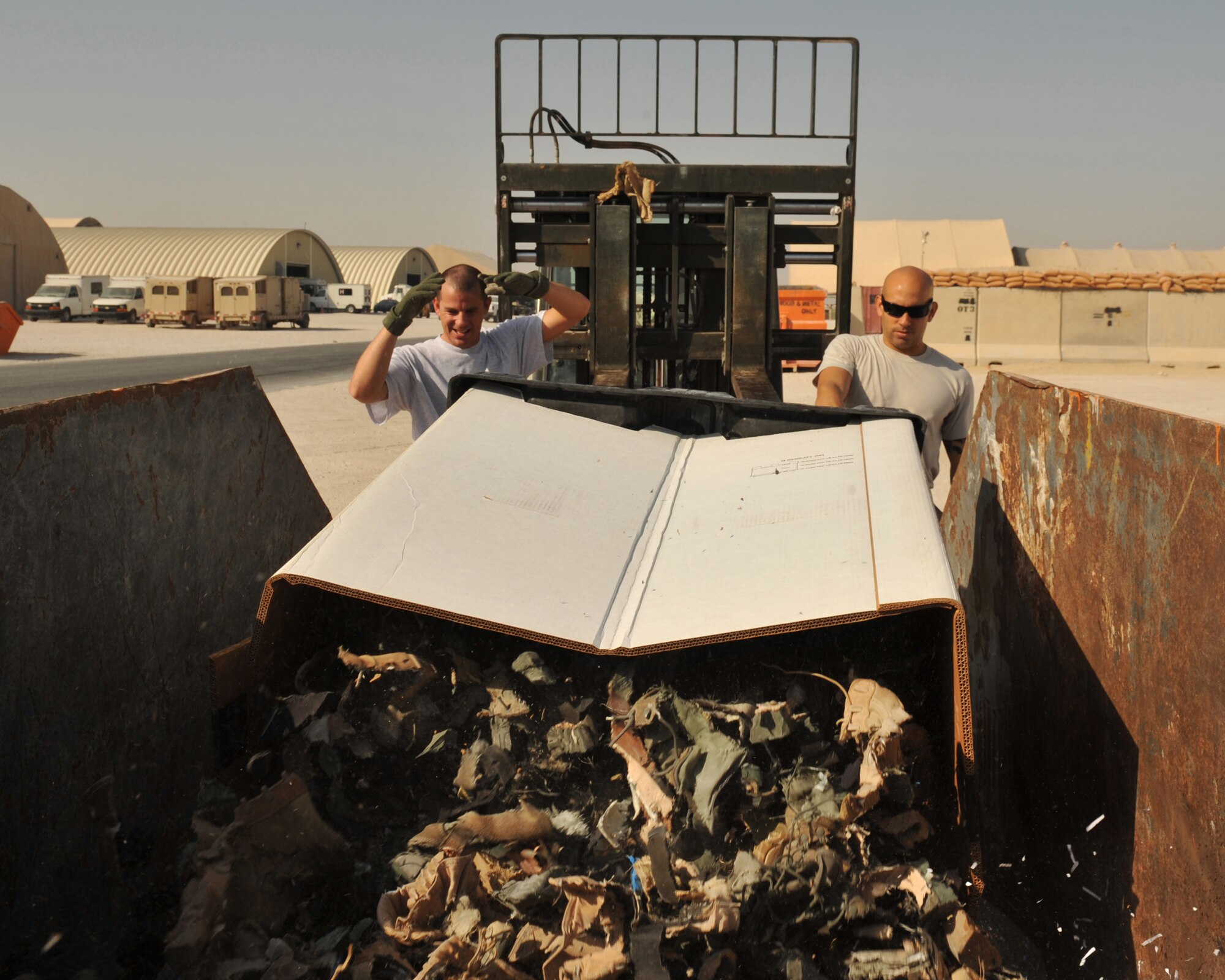 Master Sgt. Christopher Knabe and Staff Sgt. Christopher Moore dump shredded uniform items into a dumpster at the 379th Air Expeditionary Wing in Southwest Asia, Oct. 17, 2013. Military uniforms items are collected every Tuesday from drop-off locations and shredded every Thursday to maintain force protection efforts. Knabe is the 379th AEW Force Protection superintendent deployed from Misawa Air Base, Japan, and a Oklahoma City native. Moore is a 379th AEW Check Six facilitator deployed from Kadena AB, Japan, and is a Little Rock, Ark., native. (U.S. Air Force photo/Master Sgt. David Miller)