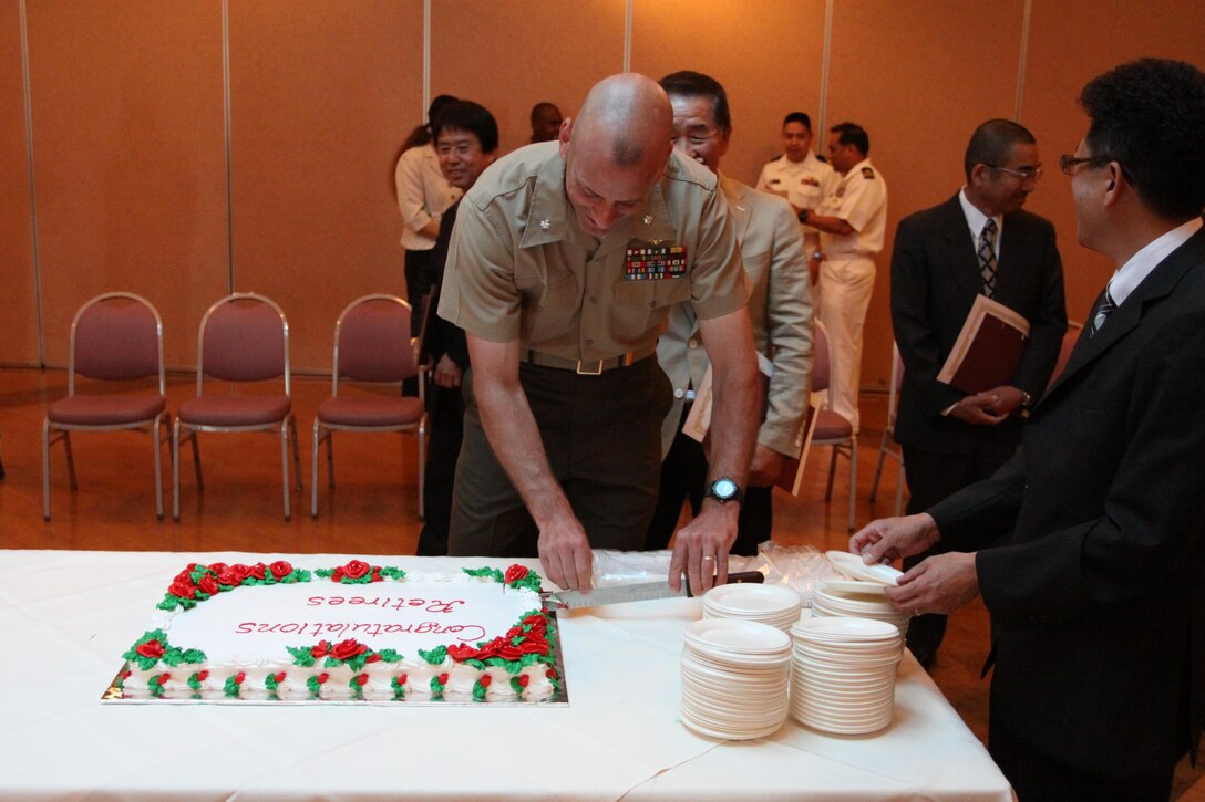 Lt. Col. Mike Carriero, Marine Corps Air Station Iwakuni S-1 and manpower director, cuts the cake after a retirement ceremony for local national employees at the Landing Zone inside Club Iwakuni, June 26, 2013. Eight local national employees received certificates for their commitment to service during the ceremony.