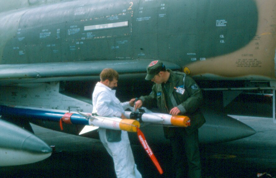 Then, Staff Sgt. Curt Shannon (right) debriefs Staff Sgt. Randy Truesdale after an F-4C proficiency load at Keflavik Naval Air Station, Iceland, in 1975.  During his military career, Shannon served as a senior enlisted advisor eight different times.  (Courtesy photo)