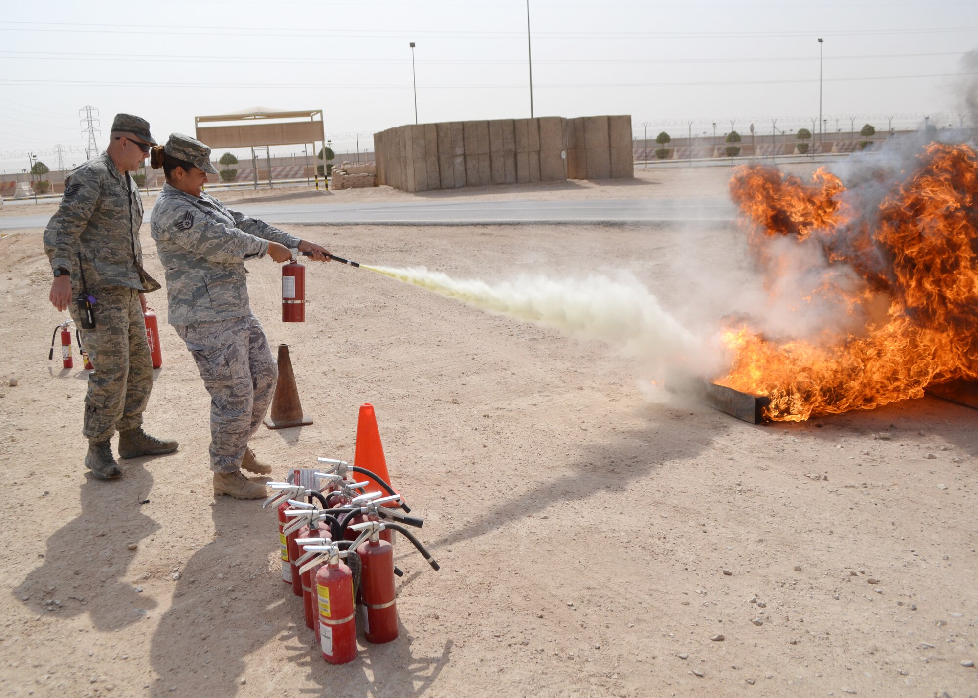 Tech. Sgt. Kurt Trausch observes as Staff Sgt. Minerva Rosario extinguishes a controlled fire during a fire prevention week demonstration at the 64th Air Expeditionary Group in Southwest Asia, Oct. 8, 2013. Rosario is a 64th Expeditionary Support Squadron plans and programs NCO in charge deployed from Barksdale Air Force Base, La., and a New York City native. Trausch is a 64th ESS Fire Prevention assistant chief deployed from Mountain Home Air Force Base, Idaho, and a Edgerton, Ohio, native. (Courtesy Photo) 