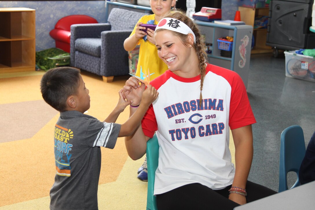 Karah Shindelar, Camp Adventure staff member, and a Japanese child show each other their paper cranes at the station’s School Age Care Center during the Minamigouchi and Kitagouchi Iwakuni city branches visit July 30, 2013. Along with other activities, Japanese children and parents taught American children how to build paper cranes.