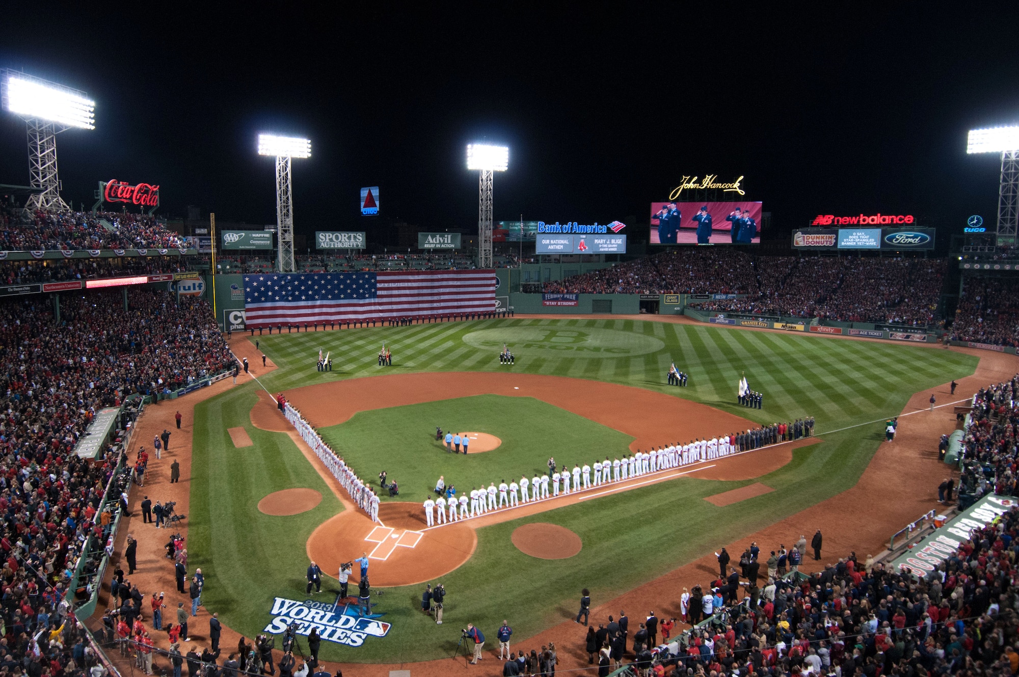 Airmen from Hanscom Air Force Base, also captured on the centerfield Jumbotron, line the flag-draped left field wall Oct. 23, 2013, at Fenway Park in Boston during the World Series opening game . Hanscom Airmen also provided one of the four military color guard formations on the field and other support to this major sporting event. 