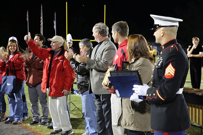 Wayne Allen, a local man, gives the crowd a thumbs up during a an award ceremony for his life savers at a football game in Jacksonville, N.C., Oct. 25, 2013. Allen recently suffered a heart attack and was saved by Baker (right), an auto maintenance technician with 2nd Maintenance Bn., Combat Logistics Regiment 25, 2nd Marine Logistics Group, stationed aboard Camp Lejeune.  (U.S. Marine Corps photo by Lance Cpl. Shawn Valosin)