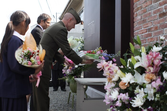 Marine Corps Air Station Iwakuni Commanding Officer Col. James C. Stewart, British consulate general of Osaka Consul-General Simon Fisher, and Mukaishima Chuo Elementary School first grader Aoi Ode, lay bouquets of flowers April 15, 2013, at the memorial site for POWs who were captured or killed at the former Mukaishima POW Sub-Camp No. 4. The part of Onomichi where the memorial stands was once known as Mukaishima, and it is here where more than 200 Allied servicemembers toiled in shipyards carrying materials until the war’s end in 1945.