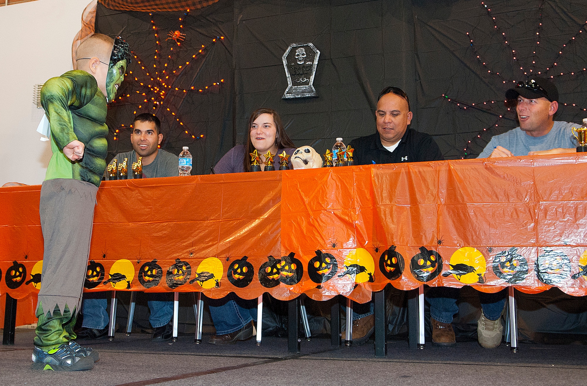 Judges get a pose from the "Incredible Hulk" during the "Trick-or-Treat-off-the-Street" event Oct. 26, 2013 in the Fall Hall Community Center. Of the nearly 600 attendees, approximately 200 children and adults participated in the costume contest based on age categories. There was also a free spaghetti buffet, haunted house, pumpkin carving contest, Trunk or Treat, carnival games and bouncy castles. The costume contest winners were: ages 0-3, Landon Knight as “Chucky;” ages 4-7, Karleyann Stephens as “‘80s girl;” ages 8-12, Esai Comes as “Boy with E.T.;” ages 13-18, Aaron Gootee as “Mummy;” and family group, the Fehlberg family as “Fairies.” (Photo by 1st Lt. Eydie Sakura)