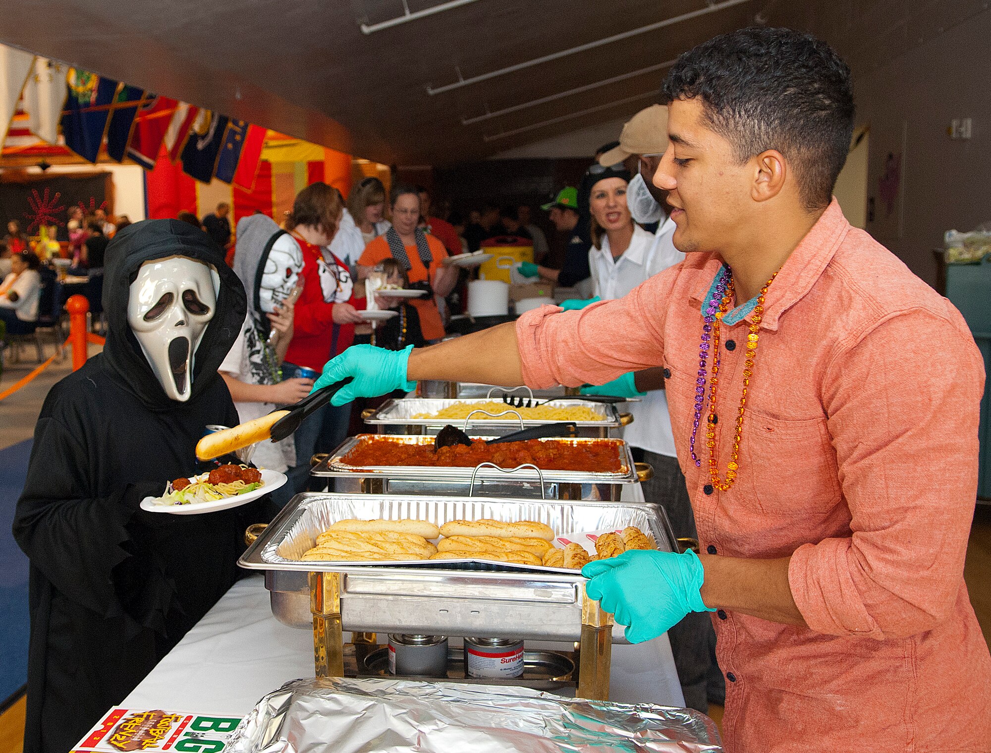 Airman 1st Class Mark Nelson, 90th Missile Security Forces Squadron, volunteers to serve food to costume-clad participants during the "Trick-or-Treat-off-the-Street" event Oct. 26, 2013 in the Fall Hall Community Center. Of the nearly 600 attendees, approximately 200 children and adults participated in the costume contest based on age categories. There was also a free spaghetti buffet, haunted house, pumpkin carving contest, Trunk or Treat, carnival games and bouncy castles. The costume contest winners were: ages 0-3, Landon Knight as “Chucky;” ages 4-7, Karleyann Stephens as “‘80s girl;” ages 8-12, Esai Comes as “Boy with E.T.;” ages 13-18, Aaron Gootee as “Mummy;” and family group, the Fehlberg family as “Fairies.” (Photo by 1st Lt. Eydie Sakura)