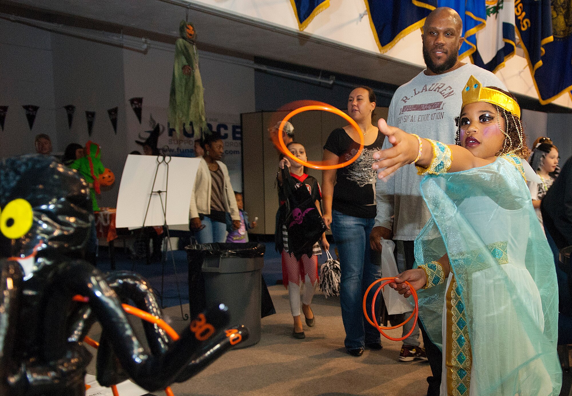 Olivia Rodgers, 7, does a ring-toss while her father, Hahsaan Marshall, waits to see what she's won during the "Trick-or-Treat-off-the-Street" event Oct. 26, 2013 in the Fall Hall Community Center. Of the nearly 600 attendees, approximately 200 children and adults participated in the costume contest based on age categories. There was also a free spaghetti buffet, haunted house, pumpkin carving contest, Trunk or Treat, carnival games and bouncy castles. The costume contest winners were: ages 0-3, Landon Knight as “Chucky;” ages 4-7, Karleyann Stephens as “‘80s girl;” ages 8-12, Esai Comes as “Boy with E.T.;” ages 13-18, Aaron Gootee as “Mummy;” and family group, the Fehlberg family as “Fairies.” (Photo by 1st Lt. Eydie Sakura)