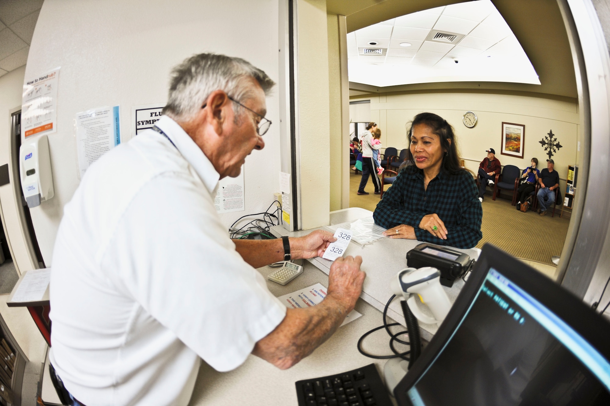 Charlie Parham, American Red Cross volunteer, assists Remy Pierce in the customer service area of the Dyess pharmacy, Oct. 21, 2013, at Dyess Air Force Base, Texas. Parham is one of more than 20 volunteers who help servicemembers, dependents and retirees at the pharmacy. (U.S. Air Force photo by Airman 1st Class Kedesha Pennant/Released)