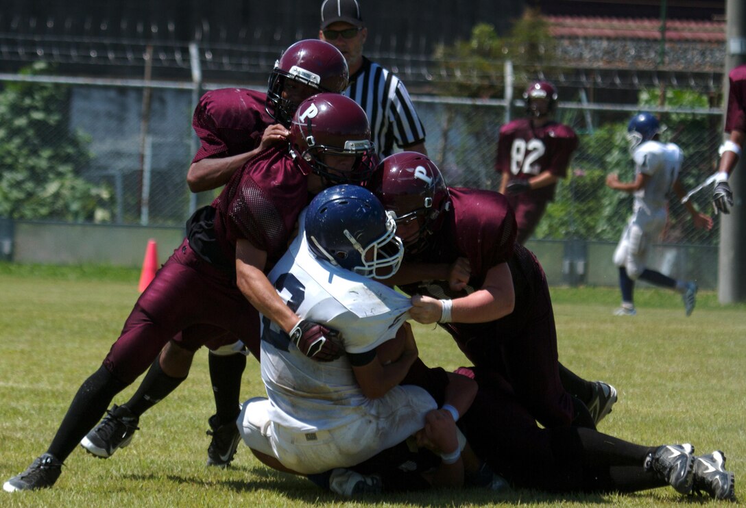 Several Matthew C. Perry High School Samurai football players swarm a Sotoku High School Fighting Ducks football player during a scrimmage at the M.C. Perry football field here Aug. 19, 2012. The scrimmage game capped off a two-day football camp between the schools where the players learned a variety of football techniques. This is the first time in eight years M.C. Perry has fielded a full-contact football team for the gridiron.