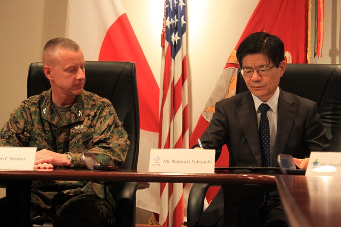 Col. James C. Stewart, Marine Corps Air Station Iwakuni commanding officer, watches as Naoyuki Fakuuchi, Osaka Regional Civil Aviation Bureau director general, signs a document during the Local Implementation Agreement Signing Ceremony, which took place inside a conference room inside Building One here, Nov. 27, 2012. On Oct. 28, 2005, the Japan/United States Joint Committe agreed to allow civil aviation operations of four round-trip flights per day at MCAS Iwakuni. The next day, the Japan and United States Security and Consultative Committee approved recommendations for the development of facilities necesssary to support said civil aviation operations.