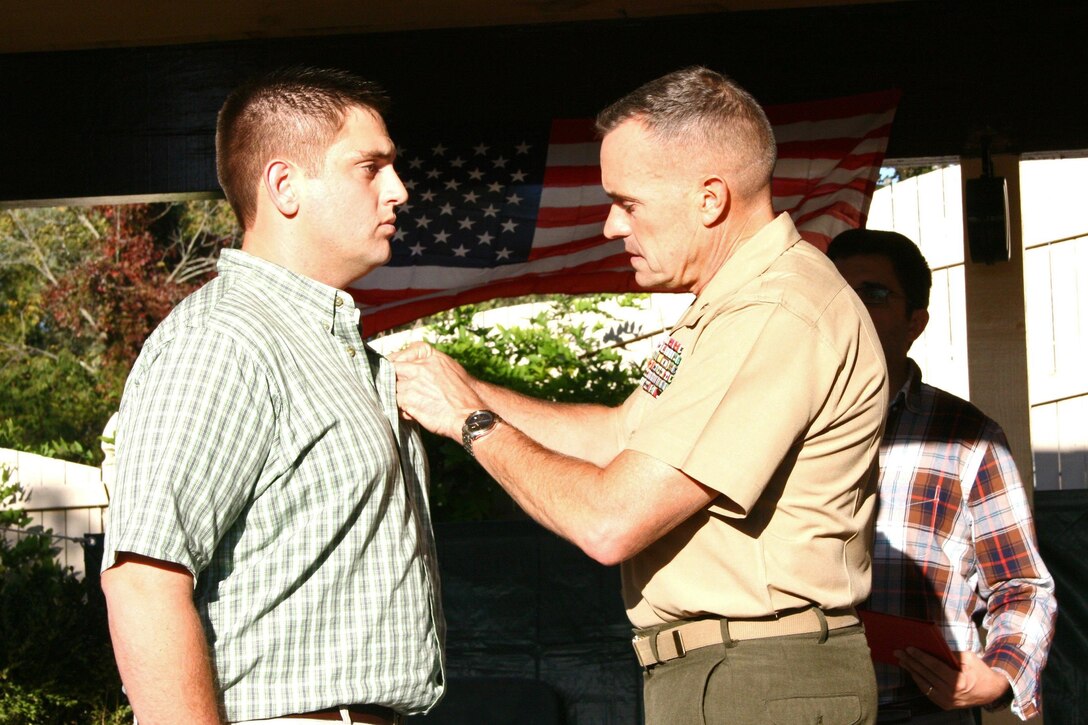 Brigadier Gen. Vincent A. Coglianese, commanding general, 1st Marine Logistics Group, pins a Purple Heart on his son, Ferdinand Coglianese, a Marine veteran, Sept. 28, 2013, in Schwenksville, Pa. While deployed with 2nd Combat Engineer Battalion, 2nd Marine Division, in Helmand Province, Afghanistan, Lance Cpl. Ferdinand Coglianese was struck by an improvised explosive device on a routine combat logistics patrol. 