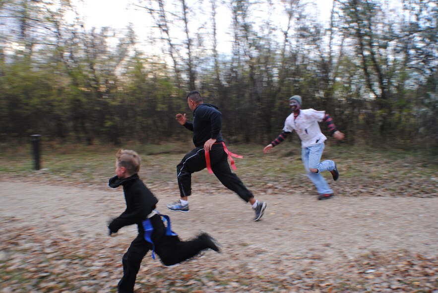 Dressed as a zombie, Senior Airman Jordan Warnke chases Lt. Col. Frank Gonzalez during the Zombie Run Oct. 26, 2013, on Grand Forks Air Force Base, N.D. The three and five kilometer runs of the event, hosted by the Air Force Sergeants Association, Chapter 964, provided a physically challenging and fun-filled event for Airmen and their families. (U.S. Air Force photo/Staff Sgt. Luis Loza Gutierrez)