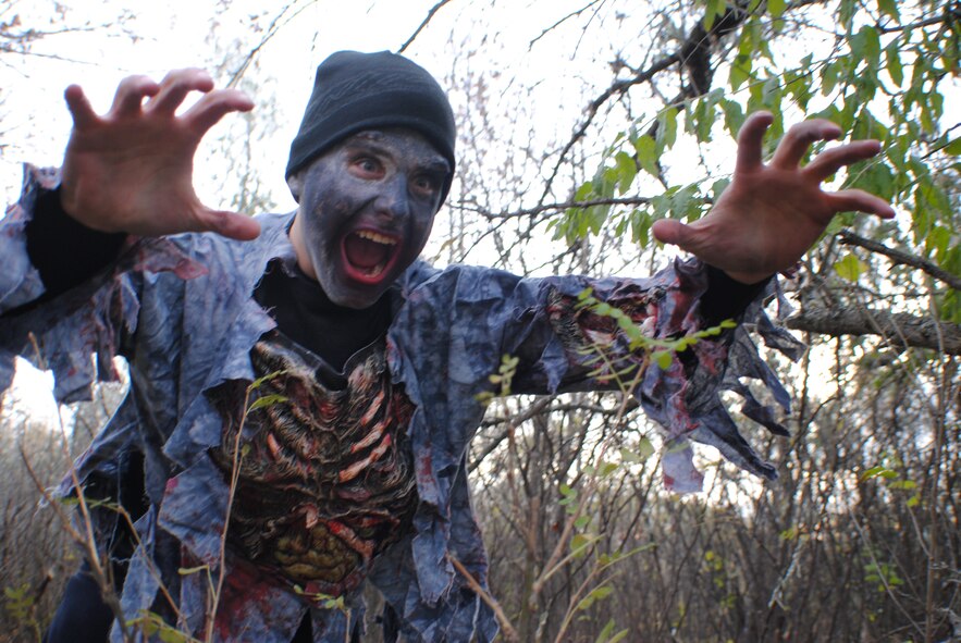 Dressed as a zombie, Airman 1st Class Raymond Booker rushes out of a wooded area surrounding a running trail during the Zombie Run held Oct. 26, 2013, on Grand Forks Air Force Base, N.D. Booker was one of 16 people who volunteered to chase runners during the event hosted by the Air Force Sergeants Association, Chapter 964. (U.S. Air Force photo/Staff Sgt. Luis Loza Gutierrez)