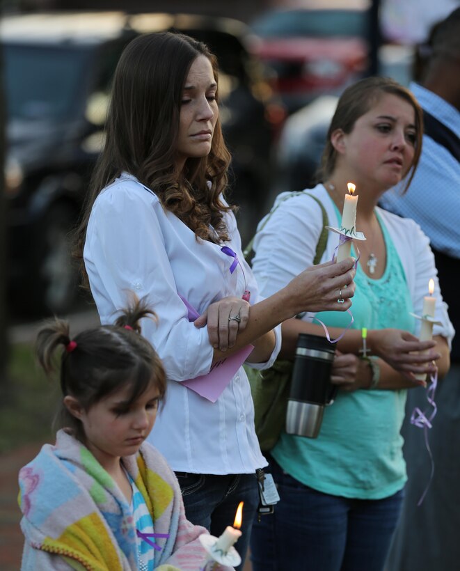 Trace Thocher (left) and Cindy Mccoy lit candles at the domestic violence candlelight vigil in downtown Jacksonville, Oct. 24. Service members rang a bell for the 52 people killed by domestic violence in North Carolina this year.