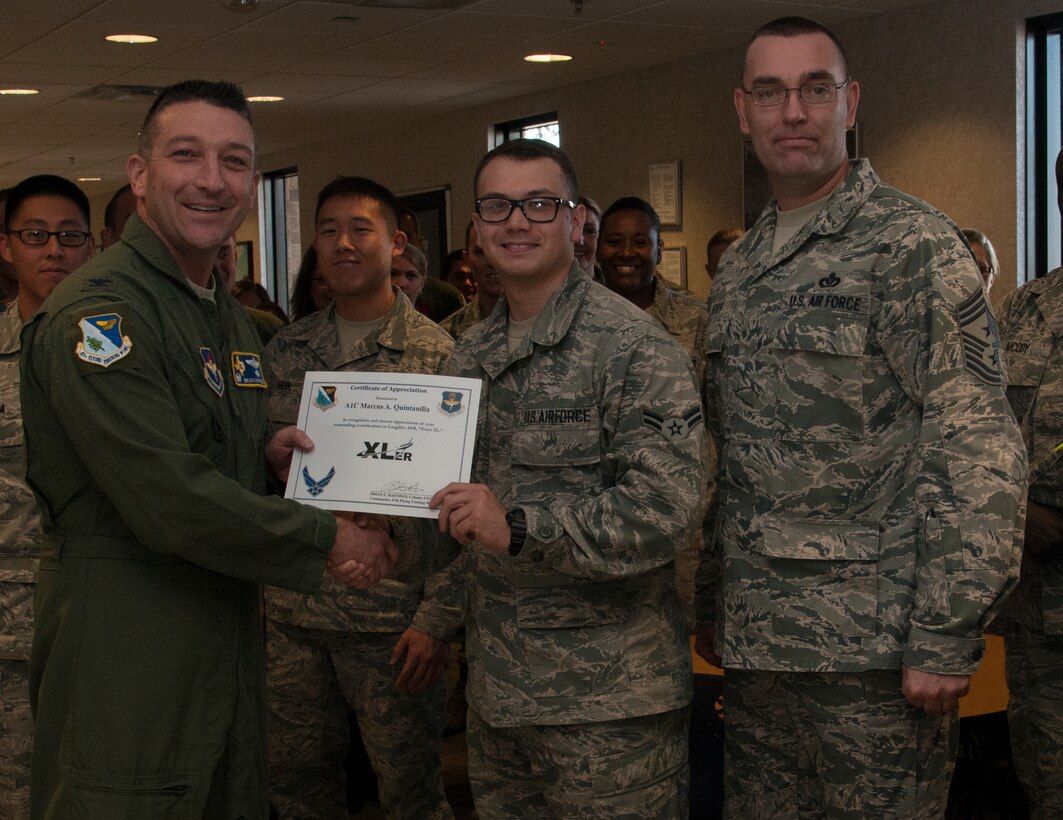 Airman 1st Class Marcus Quintanilla, center, 47th Medical Operation Squadron medical technician, poses with Col. Brian Hastings, left, 47th Flying Training Wing commander, and Chief Master Sgt. Garry Berry, 47th FTW command chief, after being presented the XLer of the week award here Oct. 23, 2013. The XLer is a weekly award chosen by wing leadership and given to those who consistently make outstanding contributions to Laughlin and their unit. (U.S. Air Force photo/Senior Airman Nathan Maysonet)