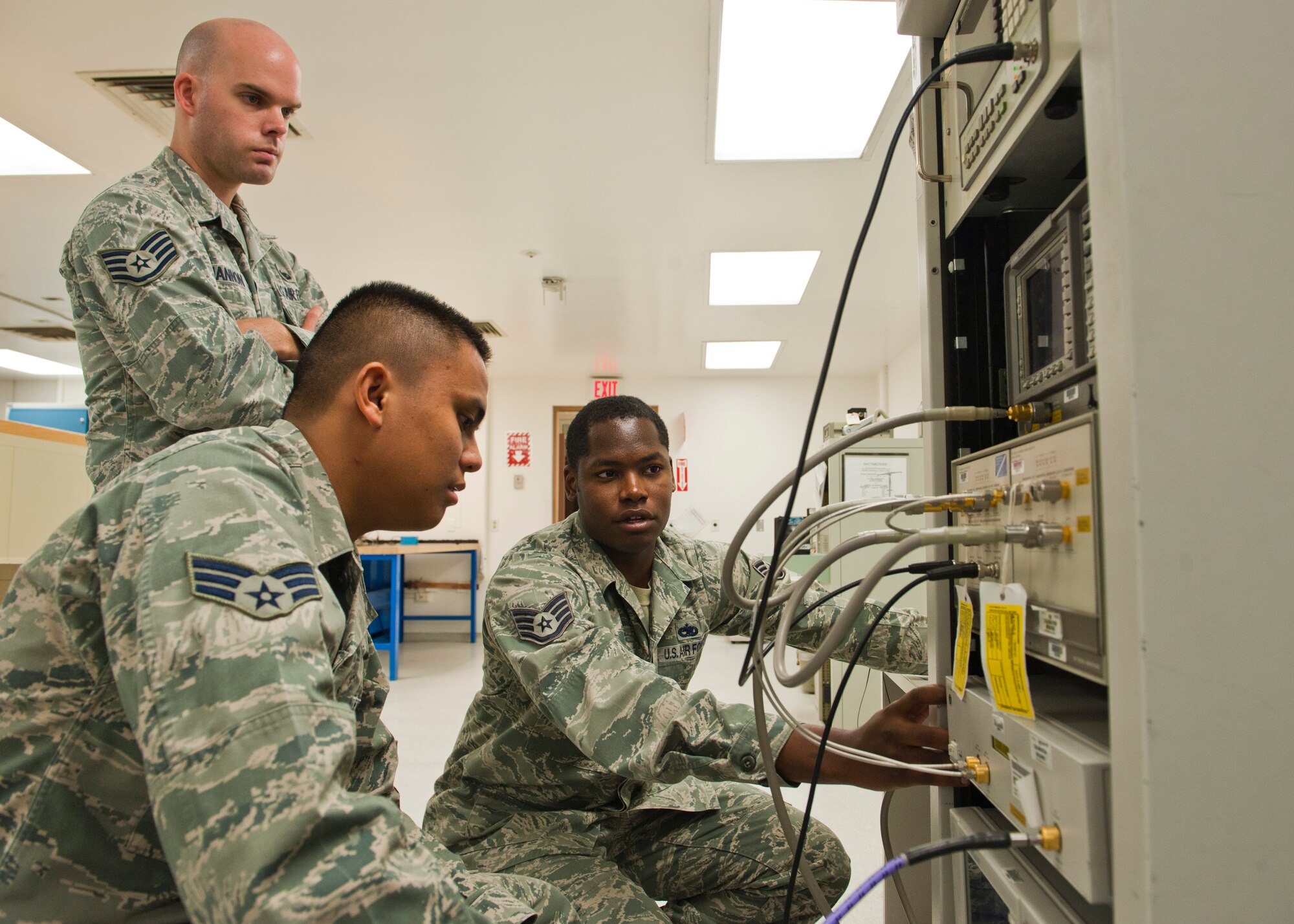 Staff Sgt. Michael Mitchell (right), 57th Maintenance Squadron Precision Measurement Equipment Laboratory craftsman, trains Staff Sgt. Christopher Hannon (standing), 57th Maintenance Squadron PMEL craftsman, and Senior Airman Alfred Trinidad (kneeling), 57th Maintenance Squadron PMEL journeyman, how to use a Phase Noise Measurement System at the PMEL Oct. 28, 2013, at Nellis Air Force Base, Nev. The Phase Noise Measurement System measures the stability of radio frequency signals. (U.S. Air Force photo by Airman 1st Class Thomas Spangler)
