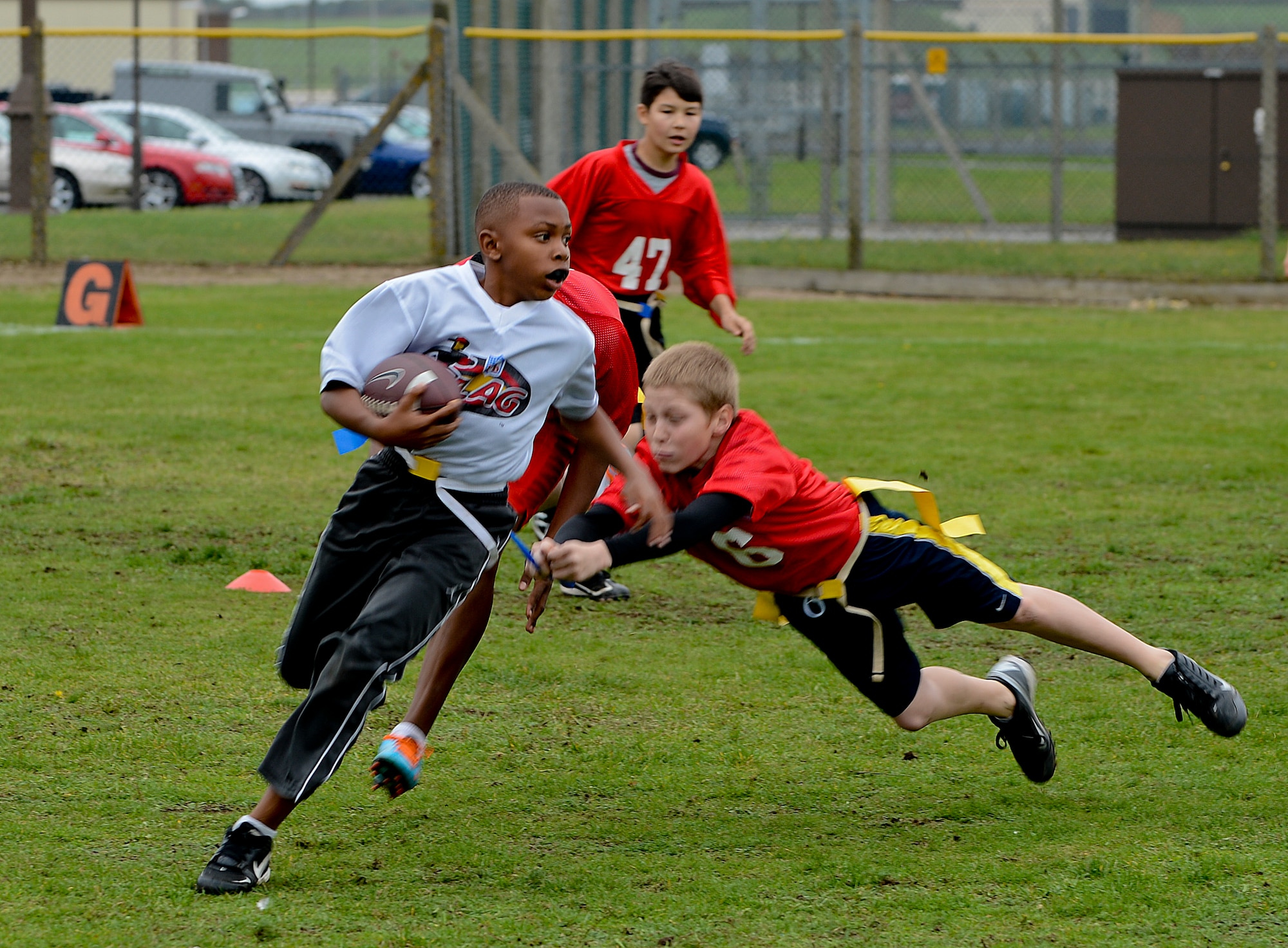 Katrell Tyre, 12, Leopards running back and son of Tech. Sgt. DeJuan Tyre, 100th Civil Engineer Squadron NCO in charge of heating, ventilation and air conditioning, runs past defenders during a flag football game at Royal Air Force Lakenheath, England, Oct. 19, 2013. The Youth Sports Program offers children 5 to 18 a wide array of organized activities to help develop physical skills, to mature emotionally and socially, and to learn the importance of teamwork. (U.S. Air Force photo by Airman 1st Class Trevor T. McBride/Released)