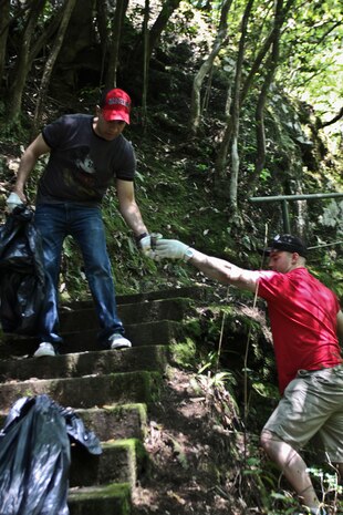 Lance Cpl. Jeffery Avery, station Provost Marshal's Office military police officer, hands a piece of trash to Pfc. Ricardo Atorgaortiz, Marine Aviation Logistics Squadron 12 Consolidated Automated Support System test station advanced maintenance technician, during the Marine Lounge Futashika River cleanup, May 18.