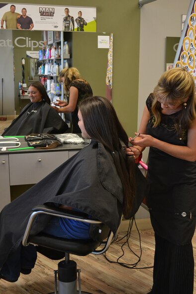 Tresha Cook, west side Great Clips manager, begins cutting banded locks of Savanna Garcia’s hair to be donated to charity.  This marks the fourth time Garcia, dependent of Melissa Laferriere, 341st Medical Operations Squadron mental health technician, and Tech. Sgt. David Garcia Jr., 341st Civil Engineer Squadron NCO in charge of pavements and equipment, has donated hair to various organizations that benefit individuals with thinning hair from cancer treatments.  (U.S. Air Force photo/Senior Airman Cortney Paxton)
