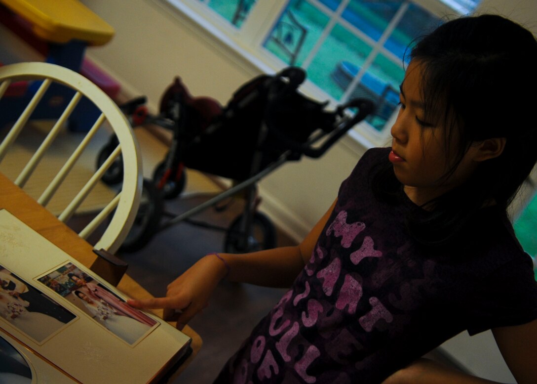 Grace Hong, 12-year-old daughter of U.S. Army Sgt. David Hong, Fort Eustis chaplain assistant, looks through her parents' wedding album at Fort Eustis, Va., Oct. 7, 2013. Grace helps her parents take care of her sister, Sophia, who has Dravet syndrome, a rare form of intractable epilepsy that begins in infancy and causes seizures and slower development.  (U.S. Air Force photo by Airman 1st Class Austin Harvill/Released)