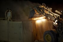 Two combat engineers with Combat Logistics Regiment 2, Regional Command (Southwest), stand on HESCO containers as a tram dumps a load of sand at Camp Dwyer, Afghanistan, Aug. 12, 2013. A platoon of combat engineers and heavy equipment operators worked through the night and endured the constant sting of blowing sand to erect a new guard tower at the base.