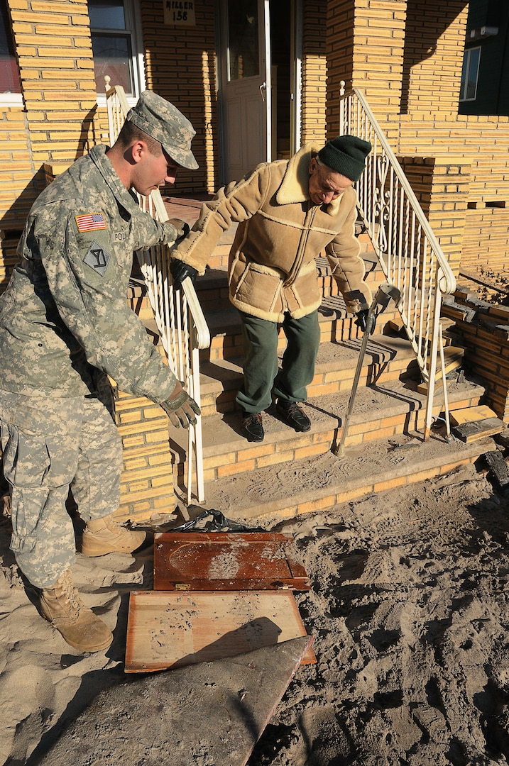 Spc. Joseph Pollini assists Leonard Miller down the steps of his boyhood home to a waiting vehicle in the Rockaway section of Queens, Nov. 6, 2012.