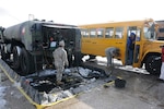 Spc. Robert Sloppy dispenses fuel to a school bus while Spc. Lauren Fratelli mans the pump valves. The two specialists, members of Delaware's aviation community, volunteered to deploy with the Delaware National Guard's 1049th as refueling specialists.