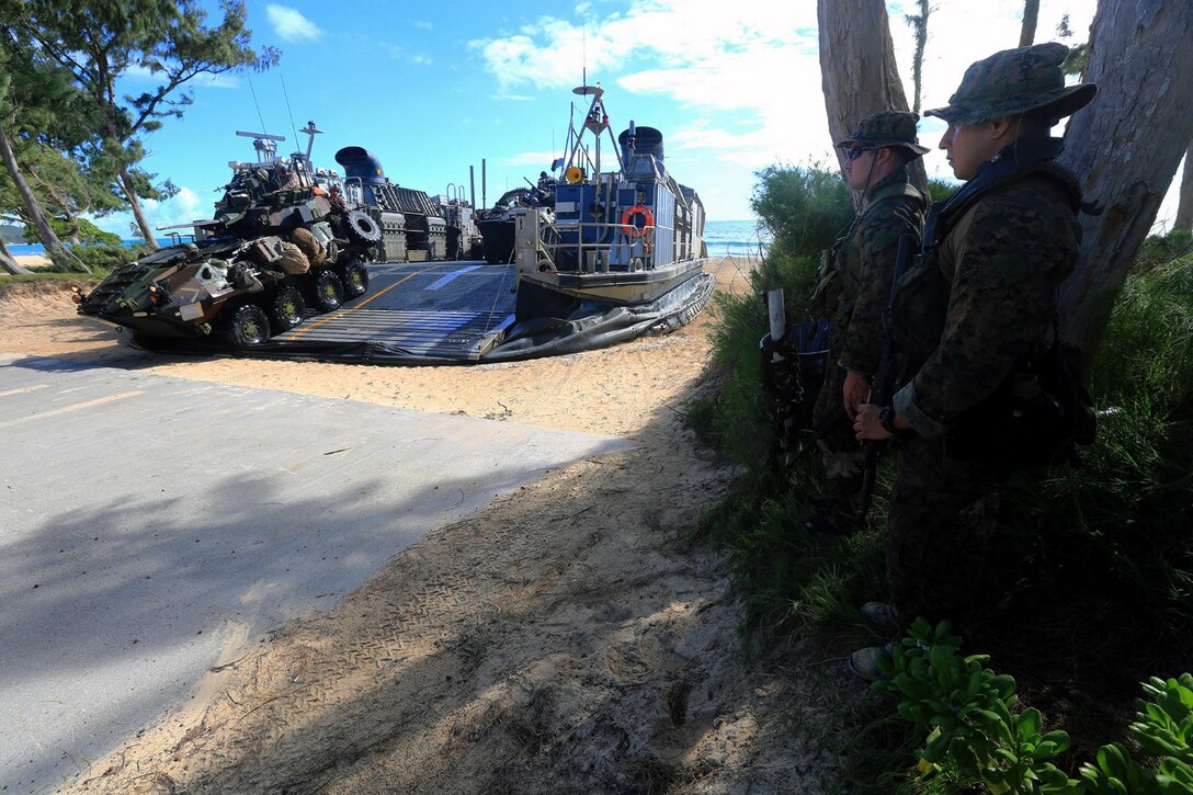 Two Reconnaissance Marines with Battalion Landing Team 1/4, 13th Marine Expeditionary Unit, provide security while a Light Armored Vehicle (LAV) vehicle drives off a Landing Craft Air Cushion (LCAC) at Bellows Beach on the Island of Oahu, Hawaii, during sustainment training Aug. 31, 2013. The Marines provided security while the rest of his team secured Combat Rubber Reconnaissance Craft (CRRC’s) in the underbrush a short distance from the waterline. Three teams left the USS Boxer on CRRC’s just after sunrise with the objective of securing an area of Bellows Beach thus allowing Landing Craft Air Cushion’s (LCAC’s) to land and transport military vehicles ashore. The Marines and Sailors with 13th MEU will deploy for several months in support of theater requirements of Geographic Combatant Commanders.  (USMC Photo by SSgt. Matt Orr/Released)