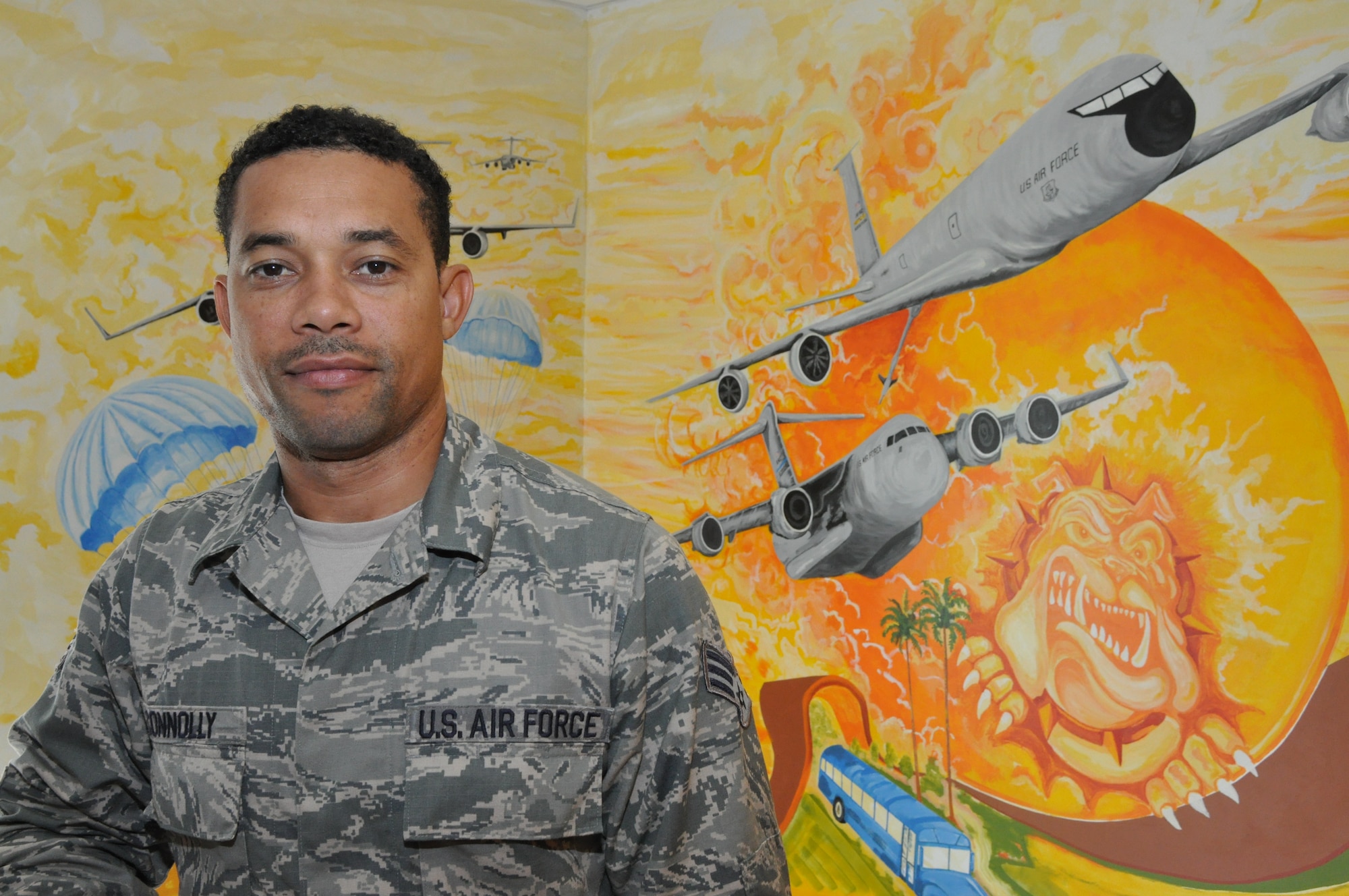 U.S Air Force Senior Airman Sean Connolly, air transportation specialist, 69th Aerial Port Squadron, poses in front of the mural he painted in the stairwell at the entrance of 69 APS here at Joint Base Andrews, Md. The mural highlights the different aspects of the aerial port mission and took more than six months for him to complete.  (Air Force Photo/ Staff Sgt. Brent A. Skeen)