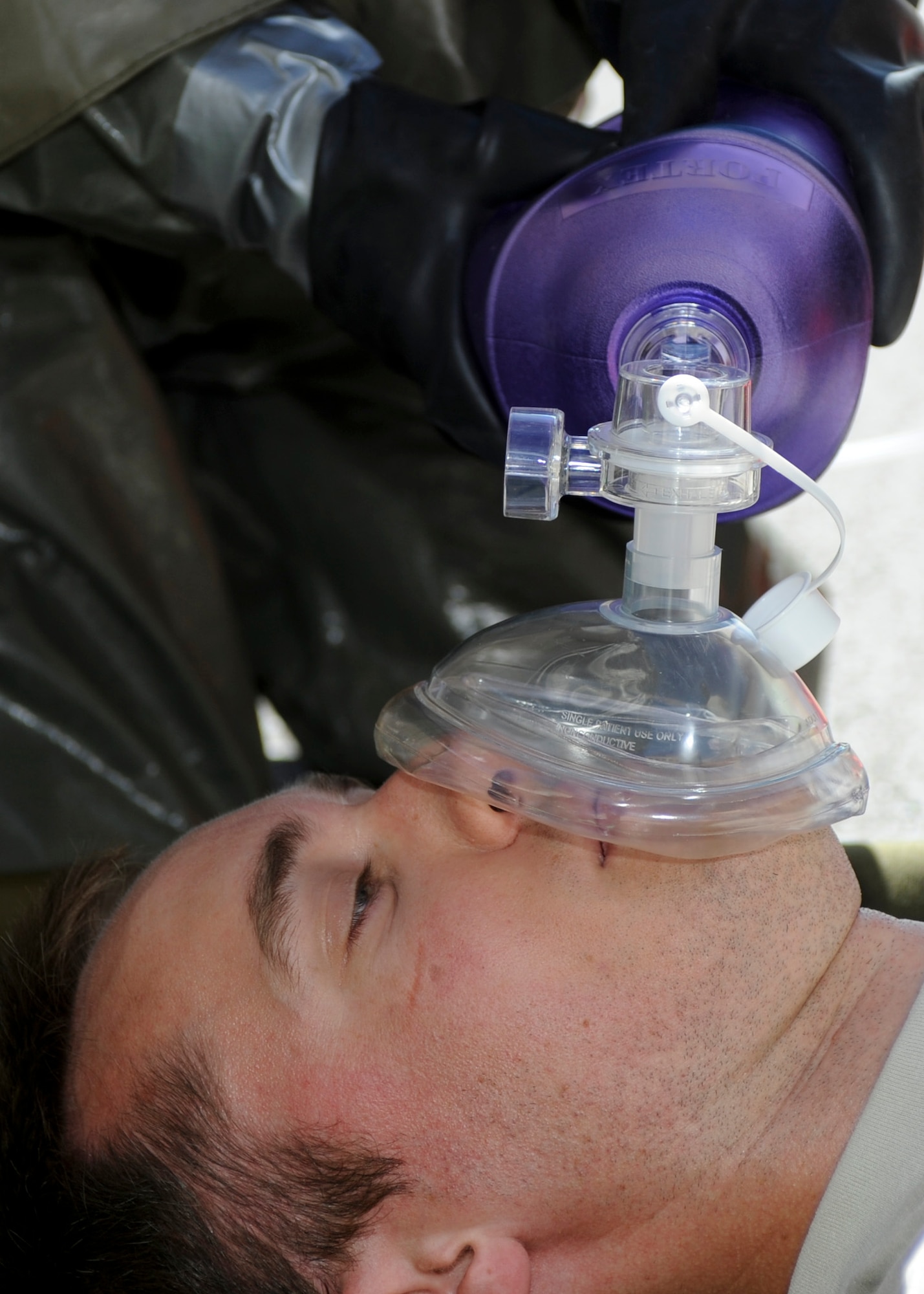 Staff Sgt. Taylor Johnson, 28th Medical Operations Squadron dental technician, simulates giving oxygen to Capt. Cory Peterson, 28th MDOS dentist, during an in place patient decontamination training exercise at Ellsworth Air Force Base, S.D., Aug. 27, 2013.  Treating life threatening injuries take precedence in the decontamination process ensuring that the victim is taken care of while also preventing contamination to medical personnel and their facility. (U.S. Air Force photo by Airman 1st Class Anania Tekurio/Released)