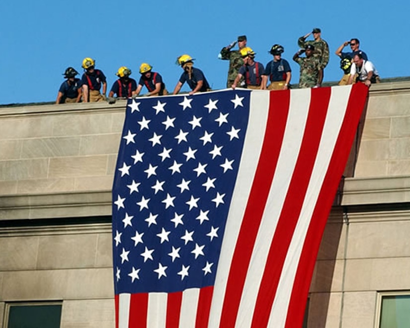 Firefighters and U.S. Army Soldiers unfurl an American flag over the side of the Pentagon during the aftermath of the 9/11 terrorist attack against the building. The Pentagon was the third U.S. building to be struck by al-Qaida militants, Sept. 11, 2001. (Courtesy photo from Reuters/Released)