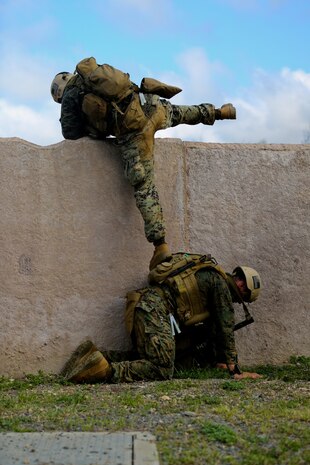 Marines serving with 1st Reconnaissance Battalion climb over a wall during a combat readiness exercise here, Aug 20, 2013. Marines responded to simulated small-arms fire and artillery fire with suppressing fire and patrols through the area. An evaluator followed each squad of Marines and assessed their various skills including tactics, coordination and execution during the mission.