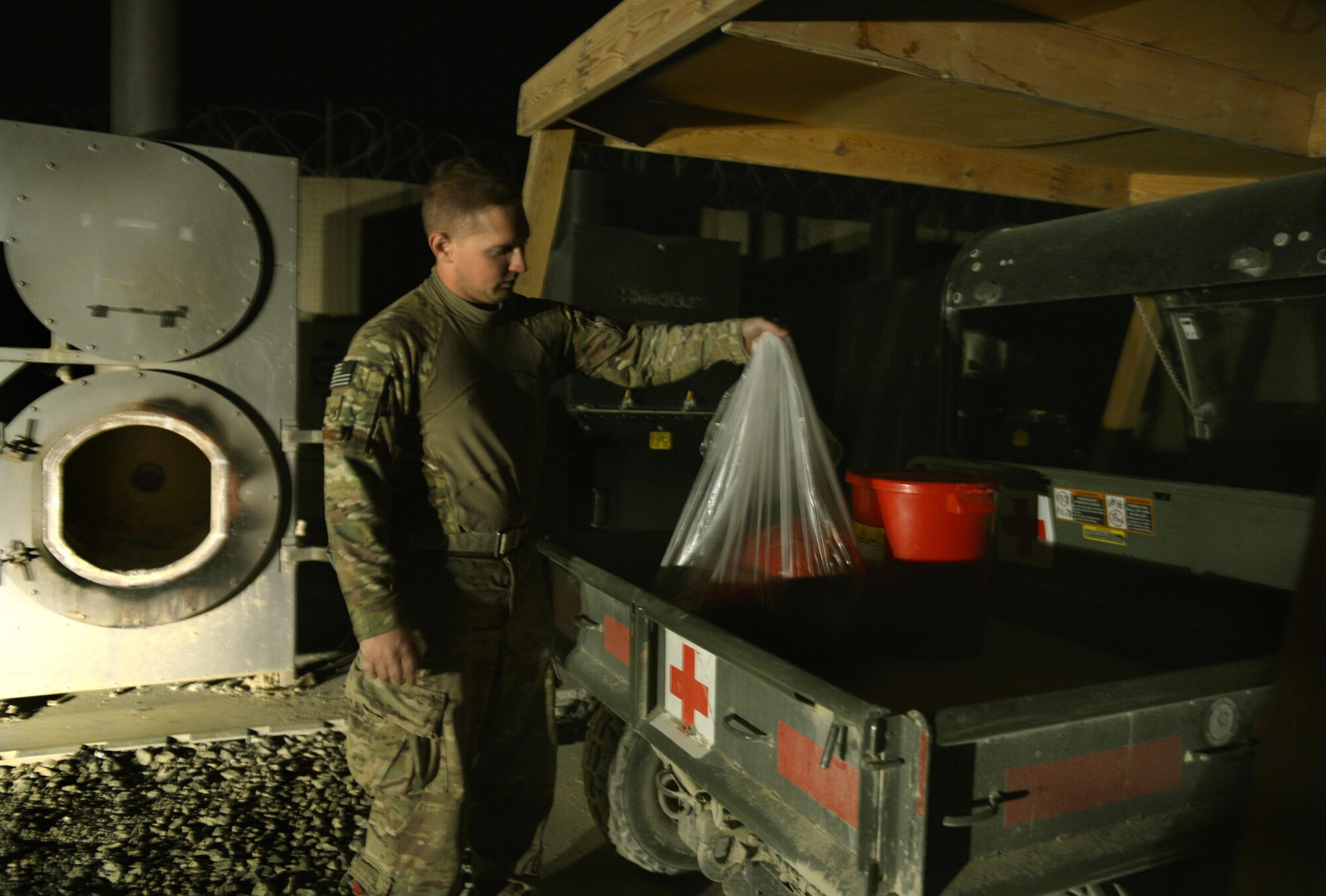 Staff Sgt. Chad Whitehead carries biowaste to put in an incinerator August 25, 2013, on the edge of Forward Operating Base Ghazni. Whitehead is a Forward Surgical Team emergency room technician and NCO in charge of Mortuary affairs. Whitehead identified and corrected issues with the incinerator that now allows the medical staff to dispose of biowaste locally. (U.S. Air Force photo/Staff Sgt. Stephenie Wade)