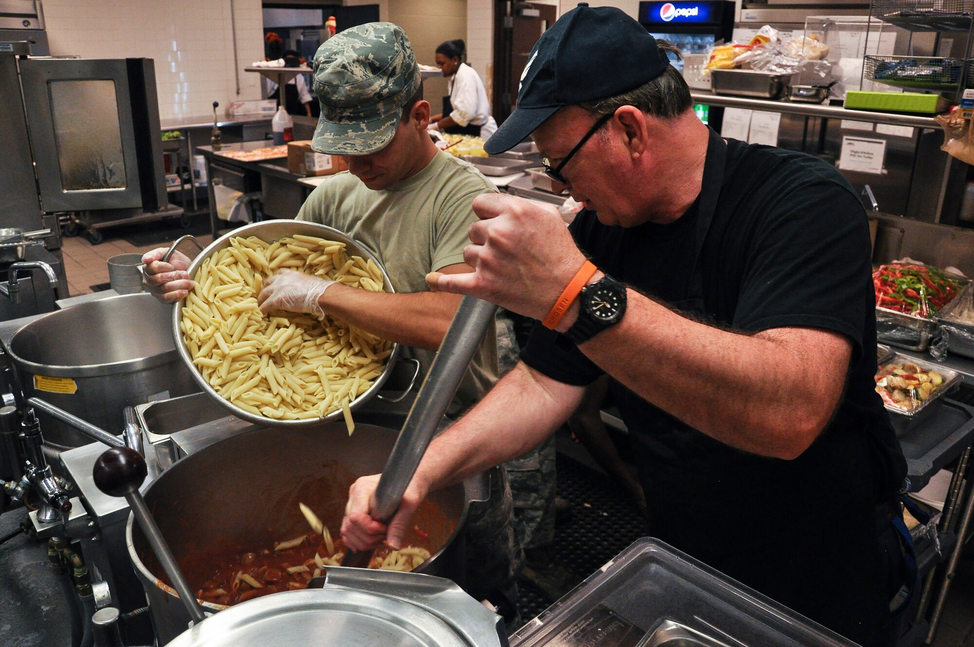 Senior Airman Adam Watson, a 19th Force Support Squadron personnel Airman, pours pasta into a pot of sauce, as Brian Lawton, a 19th FSS food services employee, stirs Aug. 21, 2013, at Little Rock Air Force Base, Ark. The dining facility hours are Monday through Sunday from 6:30 a.m. to 6:30 p.m. (U.S. Air Force photo by Senior Airman Regina Agoha)