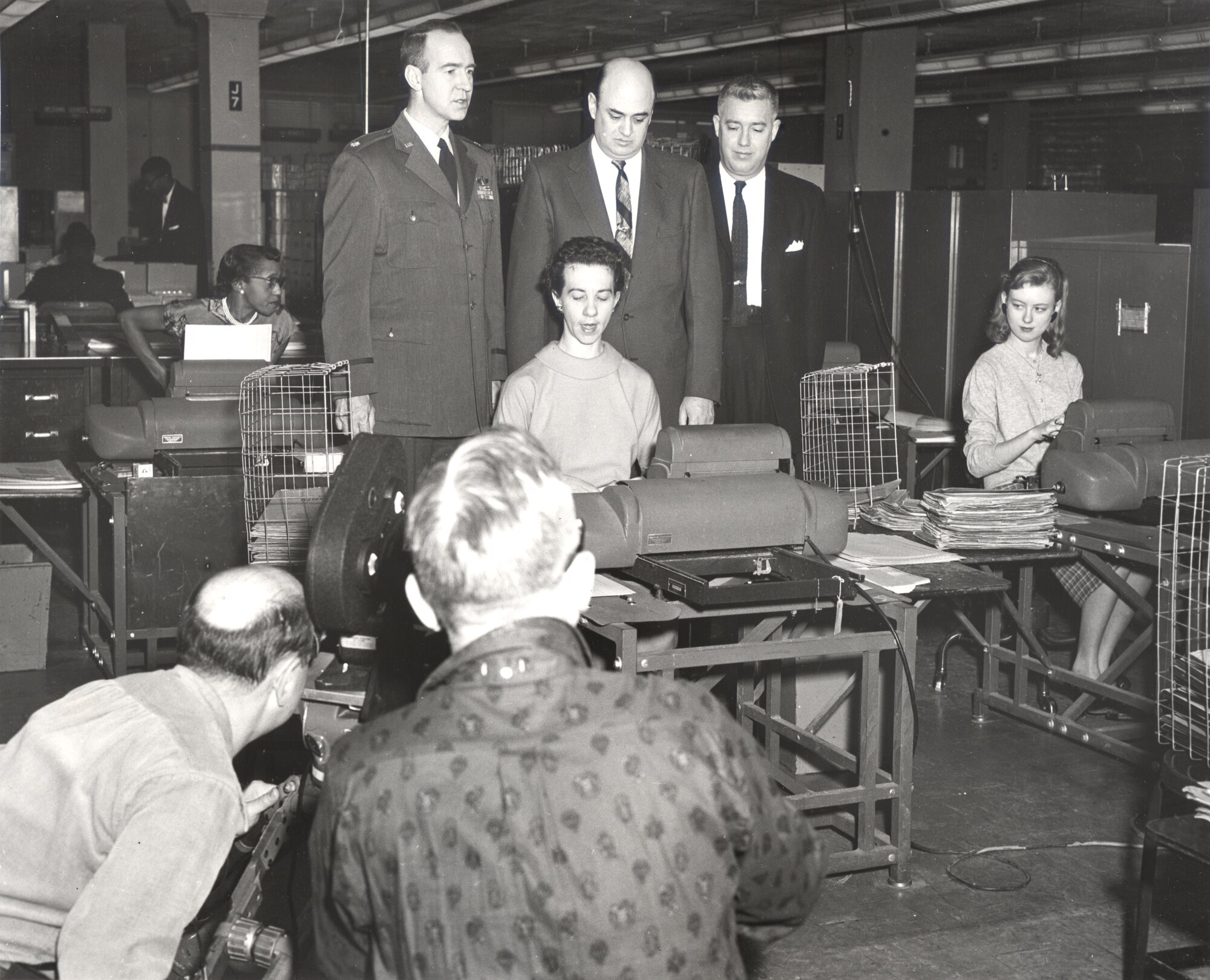 A television crew that featured the Air Reserve Records Center in a documentary filmed an employee performing her duties while senior leaders look over her shoulder at the York Street building in Denver, Colo., in 1958.
