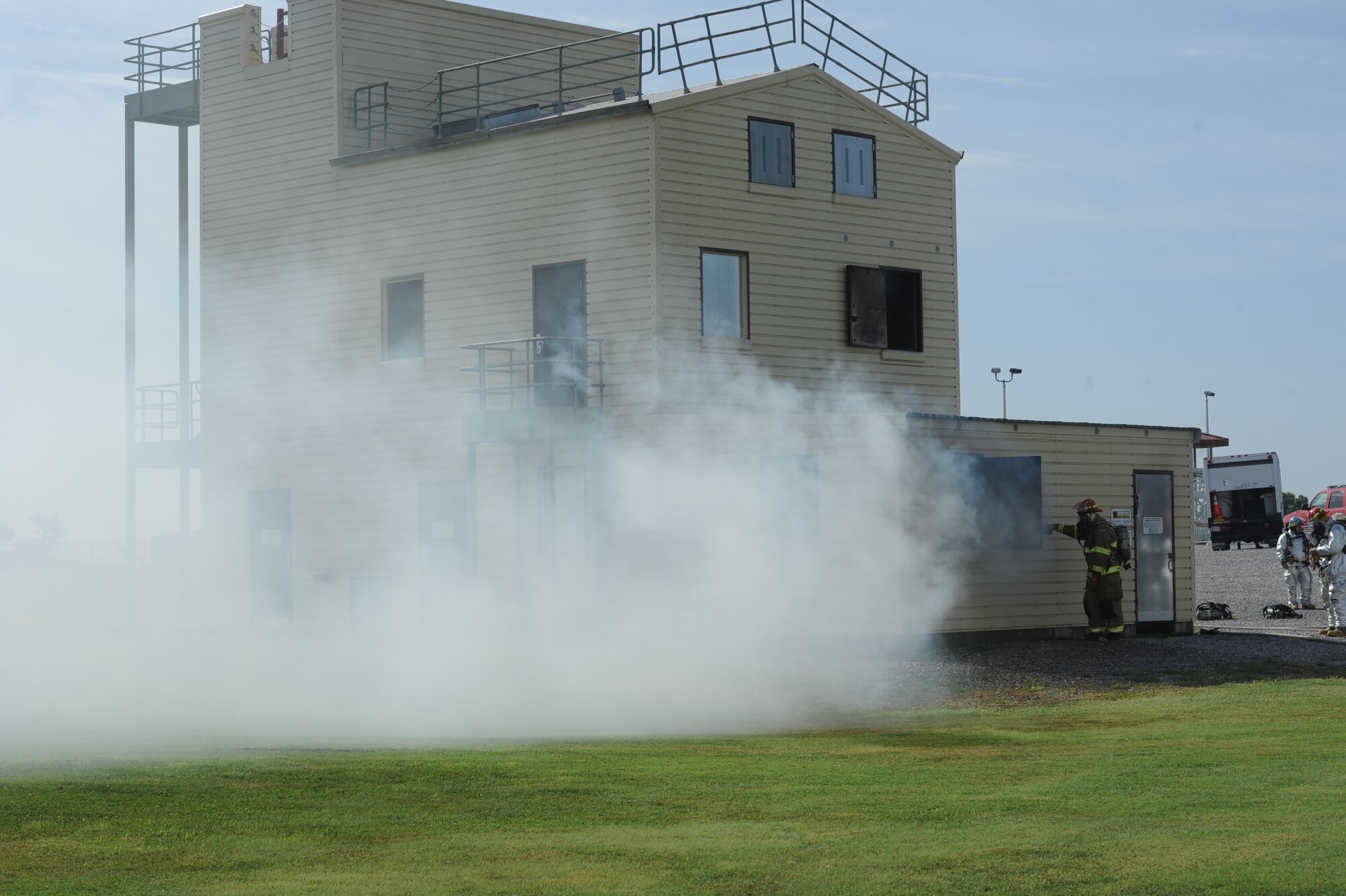Firefighters stand ready as water, smoke and steam erupt from windows of the structural burn trainer building Aug. 29 at Vance Air Force Base, Okla. The structural burn trainer is a tool firefighters use to keep their skills sharp by practicing against real fires. (U.S. Air Force photo/ Senior Airman Frank Casciotta)